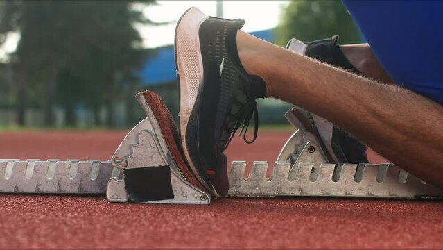 Male sprinter feet, in black sneakers, pushing off from the starting block, and start a race, close up shot.