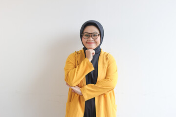 beautiful young Asian Muslim woman, wearing glasses and yellow blazer with hand on chin while smiling