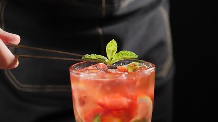Bartender putting mint leaf on fresh summer cocktail. shot on black background. Bartender decorating berry cocktail with green mint. Slow motion. Cold refreshing strawberry lemonade. Full hd