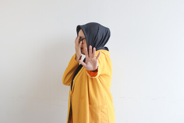 Beautiful young Asian Muslim woman, wearing glasses and yellow blazer covering 1 side of face with hand