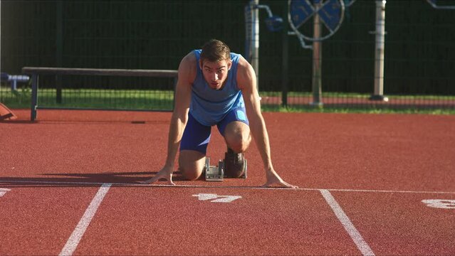 Male Caucasian young runner before the race, beyond start line in crouching start position for sprint, front view. Ready set go concept.