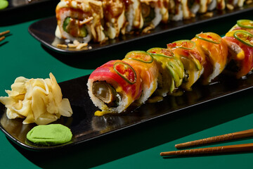 Closeup of sushi set on black plates against a vivid green backdrop, accompanied by chopsticks. Ideal for an Asian restaurant menu, casting captivating hard shadows