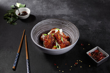 Fried Buffalo wings in Asian style on a black background. Sliced greens on wings, spices, and chopsticks in the background