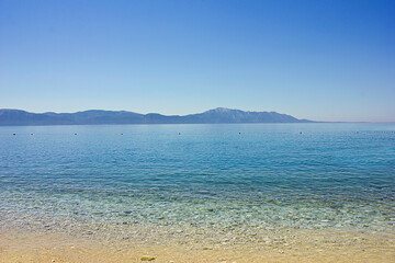 A turquoise sea with a golden beach and mountains on the horizon
