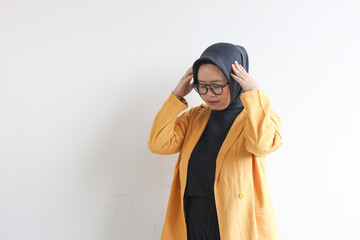 beautiful young Asian Muslim woman, wearing glasses and yellow blazer with dizzy expression holding head