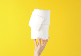 Hand holding two rolls of white toilet paper on yellow background