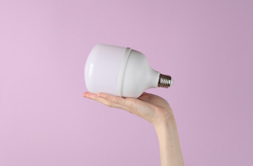 Saving electricity. Hand holding big led light bulb on purple background