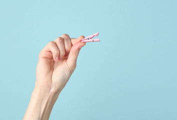 Woman's hand holding a pink clothespin on a blue background
