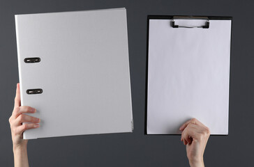 Female hands holding white binder folder and clipboard on a dark background. Business concept