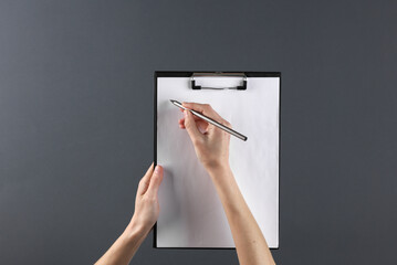 Female hands holding clipboard and writing with pen on a black background. Business concept