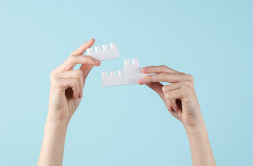 Female hands hold white blocks of children's plastic constructors on blue background. Business concept