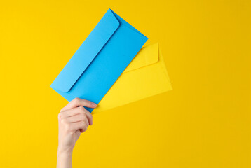 Female hand holding blue and yellow envelopes on yellow background