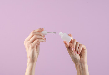 Woman's hands holding a nail balm bottle with a brush on a purple background