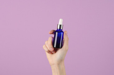 Woman's hand holding a serum bottle on a pastel background. Skin care