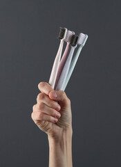 Hand holds toothbrushes on a dark gray background. Caring for teeth, oral hygiene concept