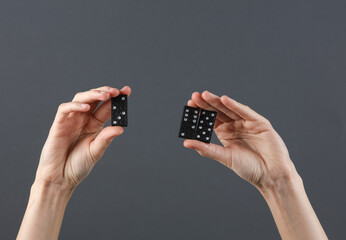 Female hands holding dominoes on a dark gray background