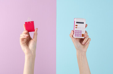 Hands holding calculator and miniature shopping bag on pink blue background. Discount, sale