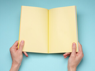 Obraz premium Female hands hold an open notebook, or a magazine with yellow blank pages on blue background