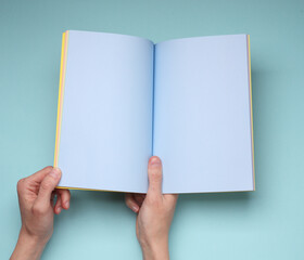 Female hands hold open notebook or magazine with blue blank pages on blue background