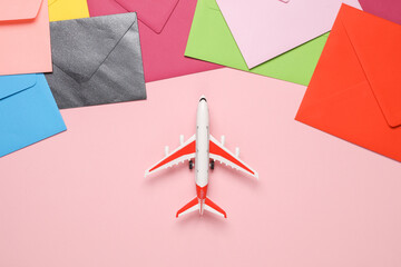 Many colored envelopes with toy air plane on pink background. Air mail, delivery