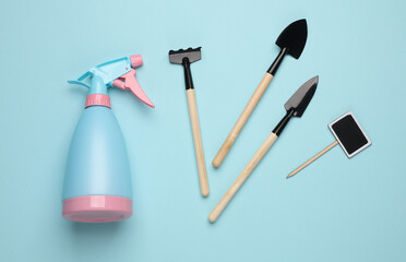 Spray bottle with mini garden tools on blue background
