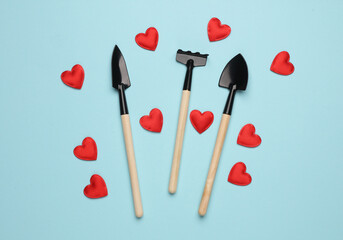 Mini garden tools with hearts on blue background. Love concept