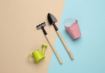 Miniature rake with a watering can, hovel with a bucket on pastel background. Gardening