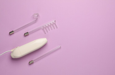 Acne treatment. Device for local darsonvalization with nozzles on a purple background. Beauty concept. Flat lay. Copy space