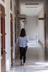 female international school student dressed in jeans walked inside school building on corridor in front of classroom alone. back of female student who was walking alone in corridor of school building.