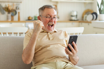 Middle aged senior man euphoric winner with smartphone. Older mature grandfather looking at cell phone reading great news getting good result winning online bid feeling amazed. Winning gesture