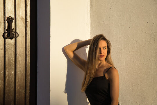 Young woman, beautiful and blonde, with black tank top receiving the last rays of afternoon sun with sensual and provocative attitude. Concept sensuality, provocation, flirting, beauty.