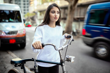 teen girl with bike and hand attached to handlebar of bicycle walk in city through cars in motion...