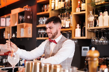 Young bartender creating a cocktail with a red bow tie. Concept: drinks, nightlife, lifestyle