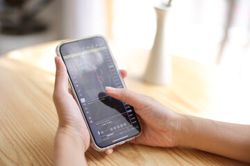 Woman hand using a smartphone for Stock exchange trading online in the coffee shop, business concept