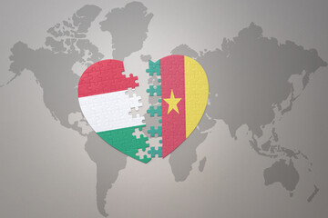 puzzle heart with the national flag of cameroon and hungary on a world map background.Concept.