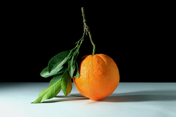 still life, close up of an orange with leaves on white table and black background