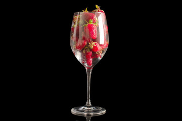 Several red strawberries in a glass goblet, macro, isolated on black background.