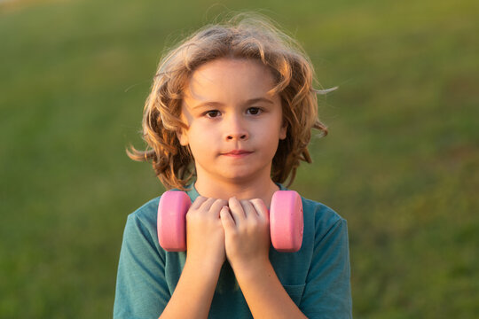 Cute little boy doing exercises with dumbbells. Portrait of sporty child with dumbbells. Happy child boy exercising. Healthy activities kids lifestyle.