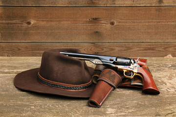 A black powder revolver in a leather holster with a leather belt next to a felt cowboy hat, on the...