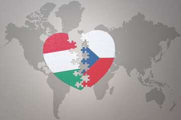 puzzle heart with the national flag of czech republic and hungary on a world map background.Concept.