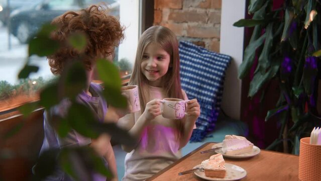 Children drinking cocoa or hot milk at cafe table with sweet desserts. Stock footage. Beautiful boy and girl communicating at a restaurant.