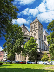 Fototapeta na wymiar Cologne (Köln), Germany - June 6. 2023: Beautiful romanesque architecture medieval german St. Kunibert church from 12th century with green trees park in summer
