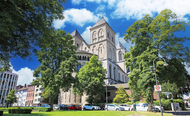 Cologne (Köln), Germany - June 6. 2023: Beautiful romanesque architecture medieval german St. Kunibert church from 12th century with green trees park in summer