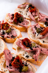 Snack bruschetta with meat, tomatoes, capers and sauce in a paper box.