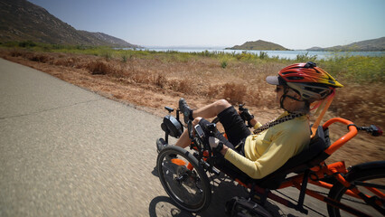 Closeup rear view of elderly senior woman riding recumbent e-bike electric tricycle bicycle on a...