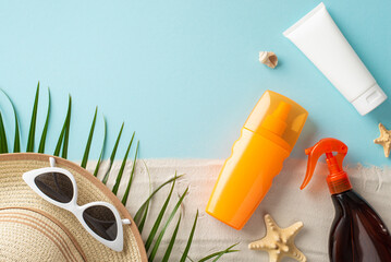 Top view arrangement of sunscreen and SPF product bottles without labels, sunglasses, sunhat, shell, starfishes, palm leaf on pastel blue and sandy surface, with vacant space for text or ad purposes