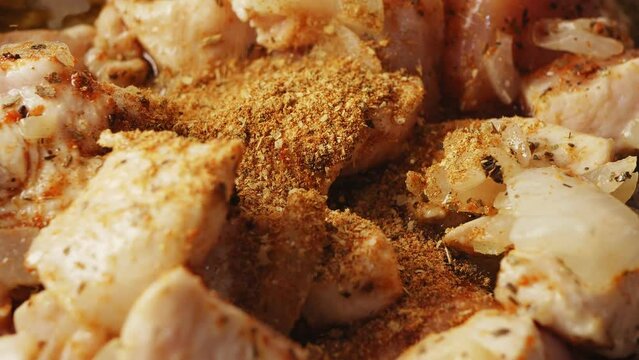 Pieces of chicken fried in a cast-iron skillet in oil with onions sprinkled with spices. Close-up