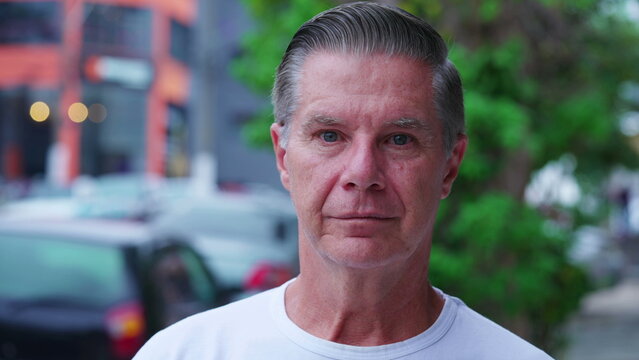 Portrait of a serious middle-aged man standing in city street looking at camera with neutral expression. Close-up face of a male older person in urban environment