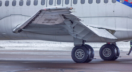 Wing of a white passenger jet airliner in winter. Photo from the side. The plane is taxiing for takeoff. Aviation lights.