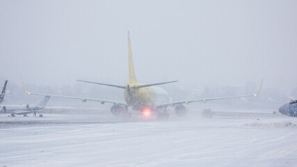 Yellow and white twin-engine passenger plane rides on the taxiway to take off in a heavy snow...